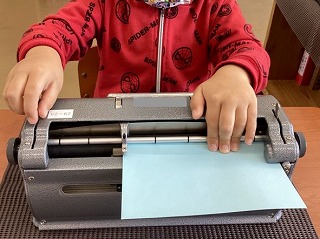 写真①点字タイプライターに点字用紙をセットする様子